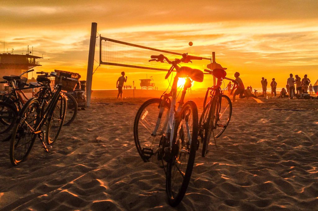 Sandy beach with sunset background, volleyball players and bikes in the foreground